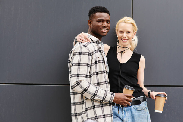 Egy multikulturális pár, egy férfi és egy nő, boldogan állnak egymás mellett egy városi utcában, egy szürke épület közelében.. - Fotó, kép