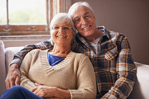 Starší pár, šťastný a portrét na pohovce s objetím, láskou a spojením v obývacím pokoji pro odchod do důchodu. Starší žena, starý muž a objetí na pohovce s pýchou, péčí a úsměvem v bytě. - Fotografie, Obrázek