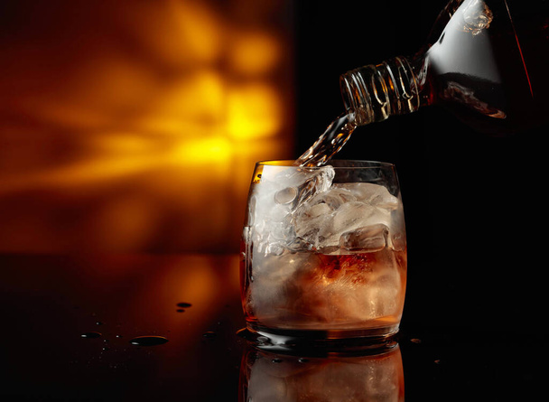 Whiskey-t önteni egy üvegből egy pohárba jéggel. Fénymásolási hely. - Fotó, kép