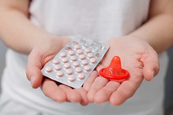 Primer plano de las manos de las mujeres con condón rojo y pastillas - Foto, imagen
