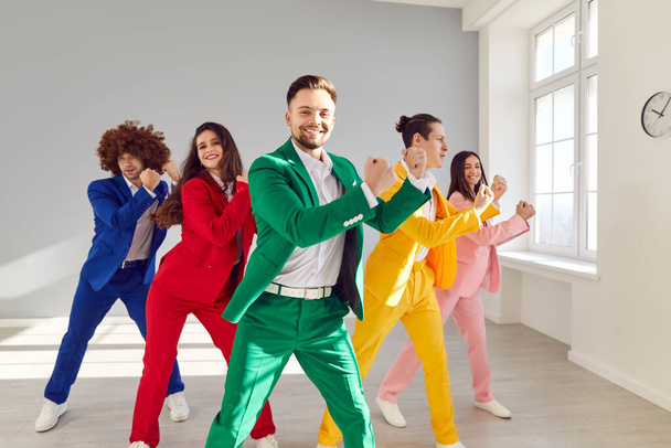 Portrait of happy cheerful dancers moving in bright suits together enjoying disco party. Five young funny friends dancing indoors in colorful fashionable costumes in dance studio indoors. - Foto, imagen