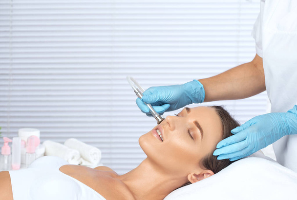 Cosmetologist κάνει διαδικασία microdermabrasion στο πρόσωπο κατά της ακμής και των μαύρων κεφαλών. Γυναικεία κοσμετολογία στο σαλόνι ομορφιάς. - Φωτογραφία, εικόνα