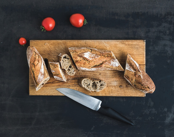 French baguette cut into pieces and cherry-tomatoes on a rustic wooden board - Foto, Imagem
