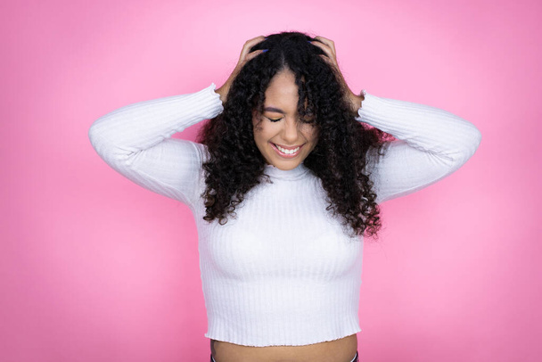 Mujer afroamericana vistiendo suéter casual sobre fondo rosa sufriendo de dolor de cabeza desesperada y estresada porque el dolor y la migraña con las manos en la cabeza - Foto, Imagen