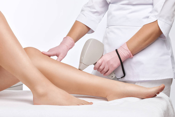 Bir kadının vücudunda epilasyon tüy çıkarma prosedürü. Güzellik uzmanı bir güzellik salonunda bacağının alt kısmında lazer gençleştirme yapıyor. İstenmeyen vücut kılları alınıyor. Donanım ipl kozmetolojisi - Fotoğraf, Görsel