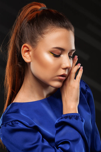 Portret van een aantrekkelijk meisje met een gezonde schone huid en mooie make-up. Ze draagt een blauwe blouse en een zwarte leren rok.. - Foto, afbeelding