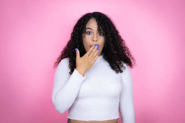 Afroameričanka v neformálním svetru přes růžové pozadí, zakrývající ústa rukou, šokovaná a vystrašená z omylu. překvapený výraz - Fotografie, Obrázek