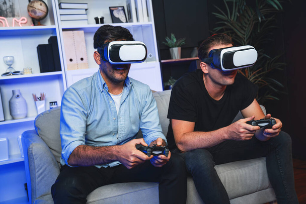 Amici amici giocatori che giocano al videogioco utilizzando joystick e VR headset di tecnologia virtuale in realtà in studio con luce blu neon. Comodo vivere al coperto con allegro vincitore di combattimento. Vendibile. - Foto, immagini