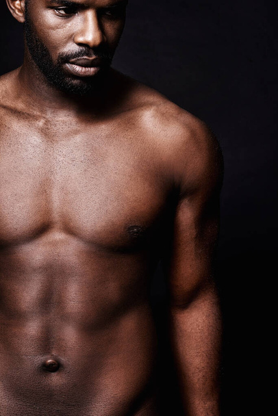 Black man, stomach and beauty on a dark background for dermatology and shadow or light with art deco or aesthetic. Cosmetics model or young person thinking in studio with shirtless abs and fitness. - Photo, Image