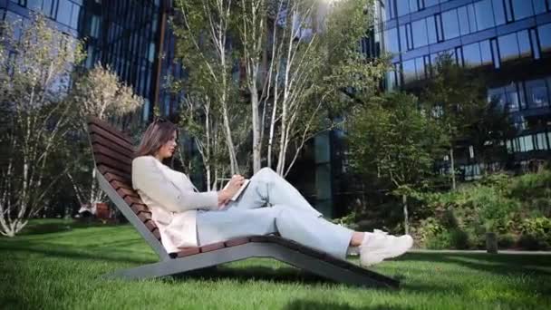 Doğa üzerine çalışan şirin bir serbest yazar not defteriyle oturuyor. Yeşil bahar parkı bahçesinde otururken ilham arıyorum. Genç bir kadın haftasını planlar ve bir günlüğe not alır. - Video, Çekim