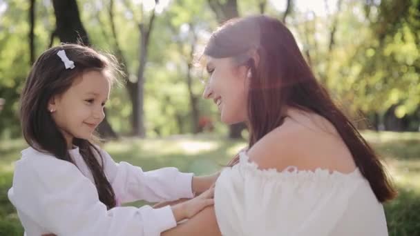 La hija abraza a su madre, tocándole suavemente el hombro. Una familia pasando un momento positivo durante un picnic en el parque - Metraje, vídeo
