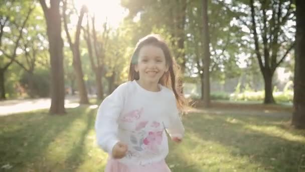 Bir parkta, küçük bir kız yeşil çimlerde koşuyor. Çocukların rüya konsepti. Gün batımında mutlu bir kız. Çocuk çayırda koşuyor. Mutlu çocuk - Video, Çekim