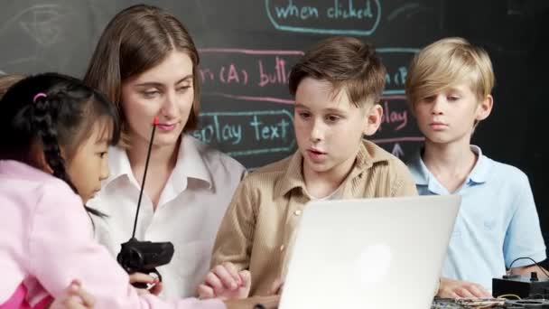 Biały chłopiec korzystający z kodu programowania laptopa i programu do pisania, podczas gdy młody nauczyciel rasy kaukaskiej trzyma kontroler w klasie technologii STEM na tablicy napisanej w trybie pilnym. Erudycja. - Materiał filmowy, wideo