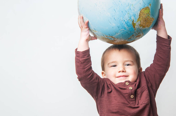 Kleine jongen houdt een bal van de wereld omhoog. De toekomst van de planeet in zijn handen.  - Foto, afbeelding