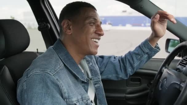 Mosolygó afro-amerikai férfi vezeti a kocsiját, és kézzel integet a barátjának a városban. Szállítás, életmód. Az emberek koncepciója. Lassú mozgás. - Felvétel, videó