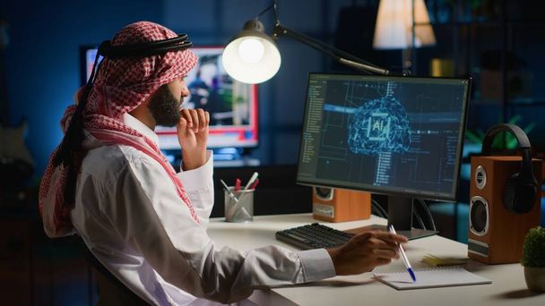 Mies kotitoimistossa kirjoittamassa näppäimistöllä, päivittämässä tekoälyverkkoja, kirjoittamassa monimutkaisia binäärikirjoituksia. Muslimi freelancer henkilökohtaisessa toimistossa päivittäminen high tech AI - Valokuva, kuva