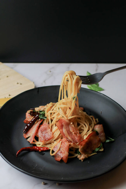 Spagetti villával, szárított chilivel és szalonnával a fehér asztalon. Hagyományos népszerű menü klasszikus olasz ételeket. Finom fűszeres ételek. - Fotó, kép