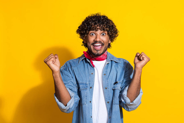 Photo portrait of handsome young guy shocked raise fists wear trendy denim garment red scarf isolated on yellow color background. - Zdjęcie, obraz