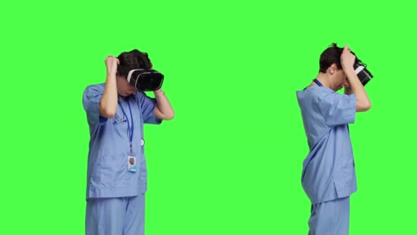 Assistente médico trabalhando com óculos de realidade virtual contra fundo greenscreen, usando visão 3d interativa no fone de ouvido vr para fazer exame de check-up. Jovem enfermeira usa gadget moderno. Câmara B. - Filmagem, Vídeo