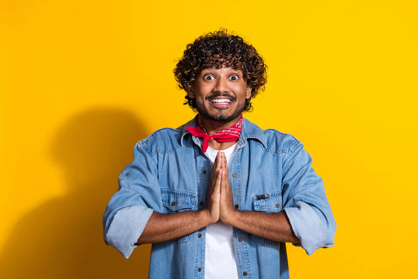 Photo portrait of attractive young man pray hands gesture wear trendy denim clothes red scarf isolated on yellow color background. - Φωτογραφία, εικόνα