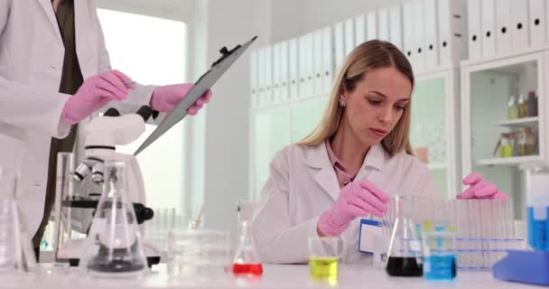 Asistente trae resultados de las pruebas a jefe científico sentado en la mesa en el laboratorio. Mujer tecnóloga recibe papeles de colega en clínica - Imágenes, Vídeo