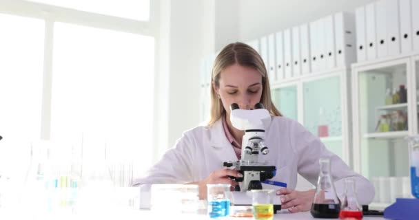 Nainen tiedemies näkee mielenkiintoisen reaktion mikroskoopilla ja soittaa kollegalleen labraan. Assistentti työskentelee suurennuslaitteen kanssa päällikön valvonnassa - Materiaali, video