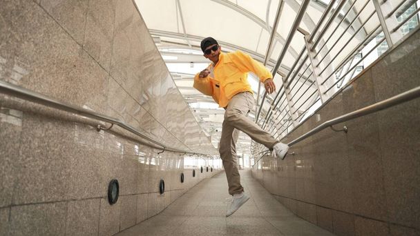 Taitava iloinen aasialainen hipsteri kävelee tanssiessaan kapealla käytävällä. Lähikuva tanssija harjoitellaan break dance esitystä. Ammattimies siirtymässä musiikkiin. Ulkoilu 2024. Sujuvasti.. - Valokuva, kuva