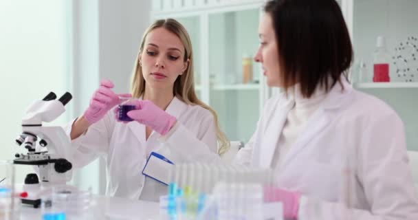 Грамотні жінки-вчені вивчають фіолетову рідину в пробірці. Досвідчені дослідники проводять експерименти на рідині в лабораторному повільному русі - Кадри, відео