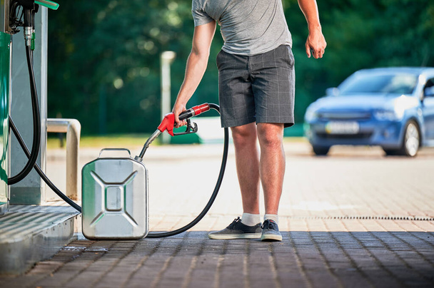 Przystojny kanister z benzyną na nowoczesnej stacji benzynowej. Człowiek napełniający cysternę paliwem w razie nieprzewidzianych okoliczności. Widok człowieka z dyszą pompy na tle samochodu - Zdjęcie, obraz