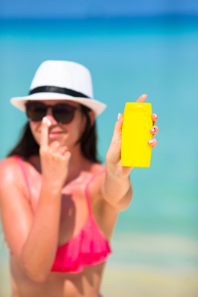 Jovem mulher feliz aplicando loção bronzeado do sol em seu nariz na praia branca - Foto, Imagem