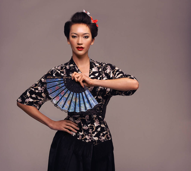 Asian woman, clothes and hand fan with confidence in studio on brown background in traditional style and elegant. Portrait, Japanese and female person with designer, fashion and outfit for heritage. - Photo, Image