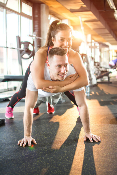 Mladý sportovní pár spolu cvičí v tělocvičně. Muž dělá cvičení prken, zatímco dívka leží na něm - Fotografie, Obrázek