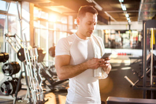 Όμορφος άντρας αποστολής κειμενικών μηνυμάτων στο smartphone στο γυμναστήριο - Φωτογραφία, εικόνα