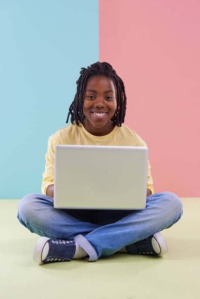Tiener, portret en laptop in studio voor online onderwijs, e-learning en creativiteit op de vloer. Kid, student of Afrikaanse jongen met computer voor school in pastelkleur of blauwe en roze achtergrond. - Foto, afbeelding