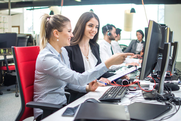 Twee lachende zakenvrouwen werken op de computer in het kantoor - Foto, afbeelding