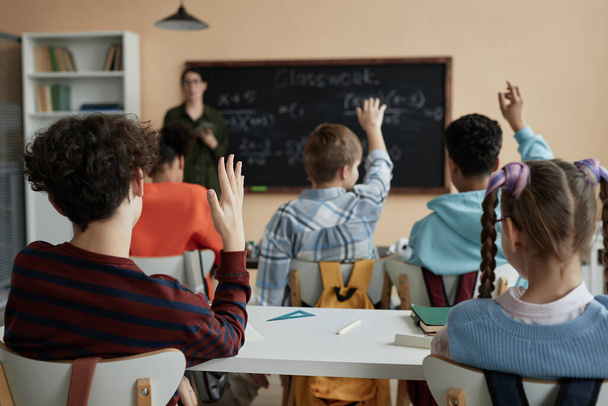 Takaisin näkymä ryhmä lapsia nostaa kätensä koulussa luokkahuoneessa ja osallistuu keskusteluun - Valokuva, kuva