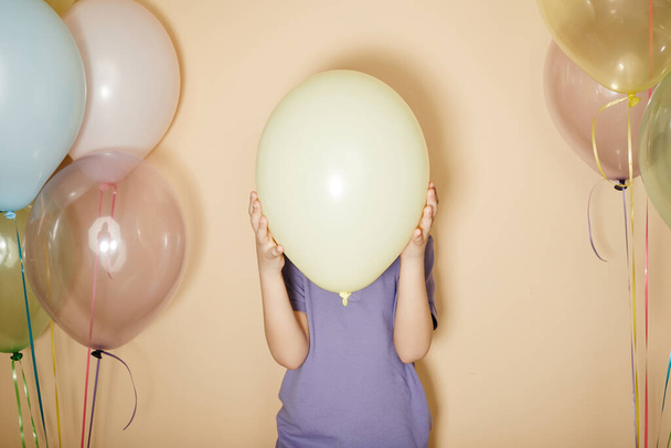 Minimální vztyčený portrét dítěte držícího balón a skrývajícího se na párty, kopírovací prostor - Fotografie, Obrázek