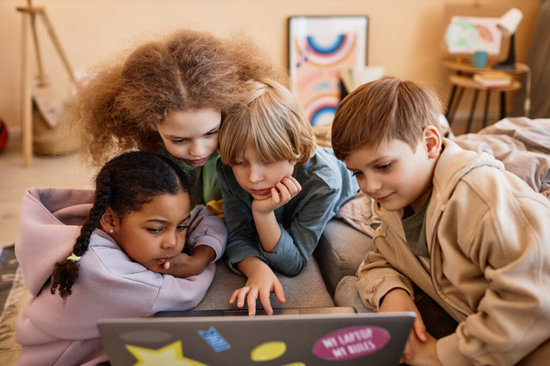Группа детей, смотрящих на экран компьютера вместе, прижавшись к ноутбуку - Фото, изображение