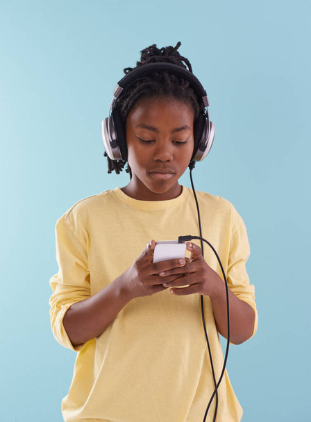 Phone, music and black boy with headphones in studio for internet, playlist or search on blue background. Smartphone, radio and teen model with app for podcast, streaming or sign up subscription. - Photo, Image