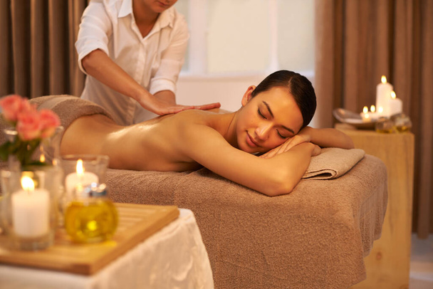 Back massage, therapist and woman relax in spa for skincare, wellness or health at table for luxury. Body, pamper or hands of masseuse at salon for beauty, peace or calm with candles for aromatherapy. - Photo, Image