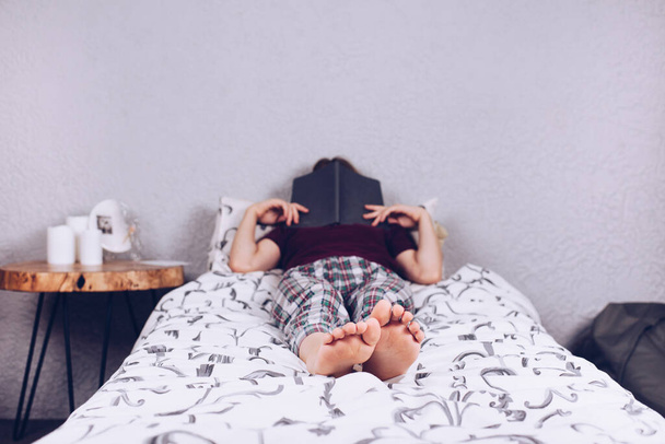 Los pies desnudos de una adolescente. La chica en pijama yace en la cama cubierta con una manta. Pie y talón - Foto, Imagen