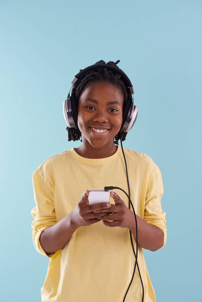 Music, phone and boy portrait with headphones in studio for internet, playlist or search on blue background. Smartphone, radio and teen model with app for podcast, streaming or sign up subscription. - Photo, Image