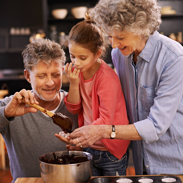 Opetus, leivonta ja isovanhemmat tytön kanssa, hymy ja ainesosat auttavat ja sitoutuvat yhteen. Perhe, vanhempi mies tai vanha nainen lapsenlapsi, onnellinen tai astiat resepti tai harrastus keittiössä. - Valokuva, kuva