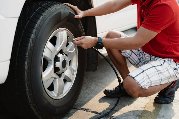 Un homme est assis sur le sol et gonfle un pneu avec un gonfleur de pneus. Concept d'urgence et importance de maintenir une bonne pression des pneus pour une conduite sûre - Photo, image