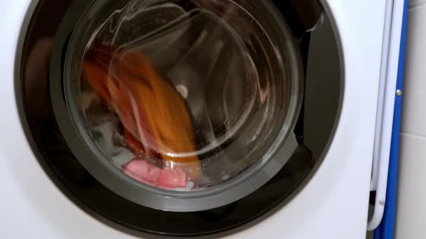 spinning drum washing machine with laundry, front loading, modern home appliances, repair. Closeup of washing machine door with spinning laundry  - Footage, Video