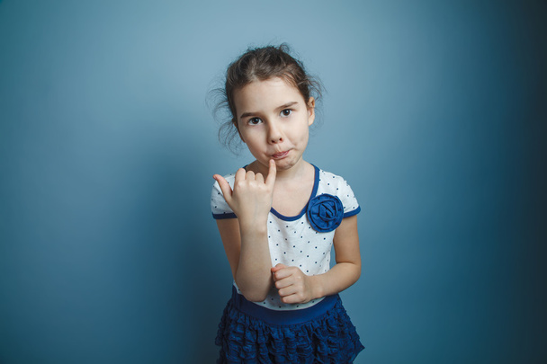 uma menina de sete aparência europeia morena lambe um dedo em um
 - Foto, Imagem