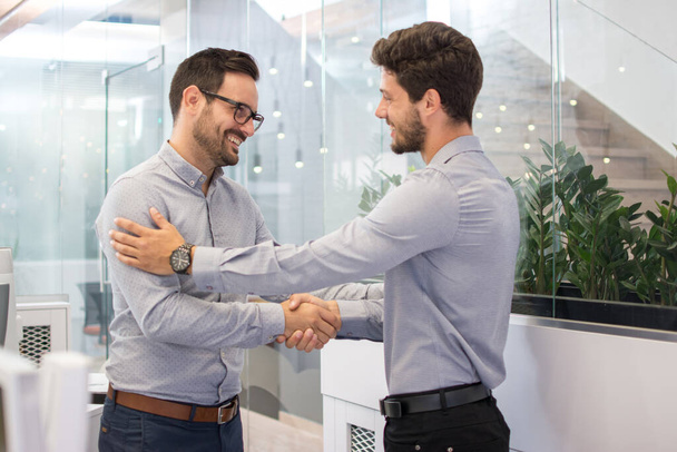 Двоє усміхнених бізнесменів трясуться разом, стоячи в сучасному офісі - Фото, зображення