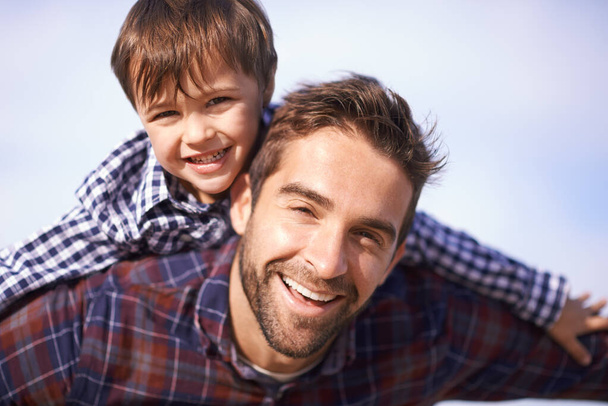 Portrait, man and child with piggy back, smile and playful travel to relax on outdoor adventure. Support, face of father and son in nature for fun bonding, playing and happy trust on holiday together. - Photo, Image