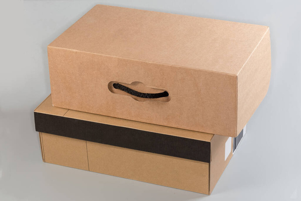 Closed kraft cardboard shoes box with rope handle lies on the other shoes box made from similar material with closed lid on a gray background - Photo, Image