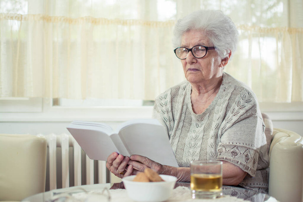 Idősebb nő könyvet olvas otthon - Fotó, kép